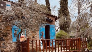 Un edificio in pietra con una recinzione in legno, una piccola porta blu e un viale lastricato in pietra.