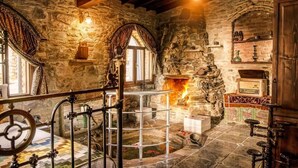 Una stanza con pareti in pietra, un camino, una scala in legno e una ringhiera in metallo.