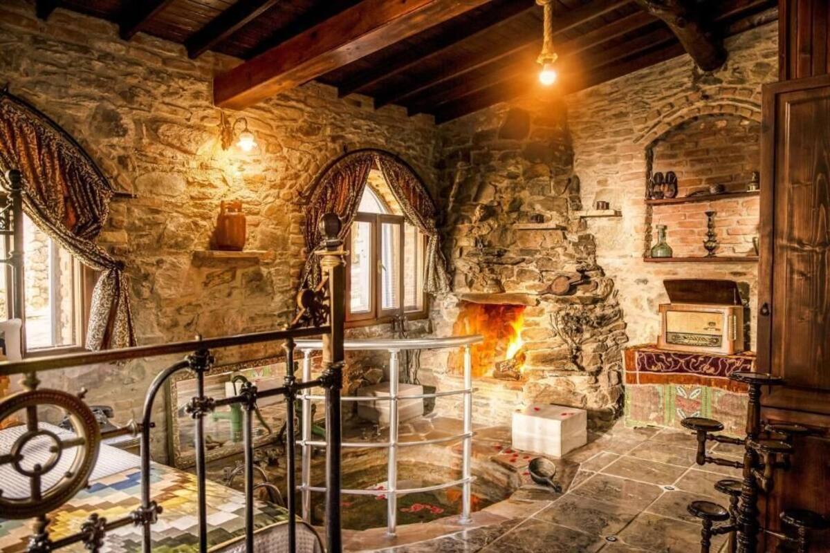 A stone-walled room with a fireplace, a wooden staircase, and a metal railing.