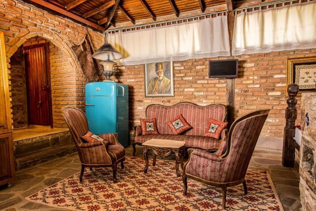 A cozy room with a brick wall, a blue refrigerator, a sofa with patterned cushions, and a wooden chair.