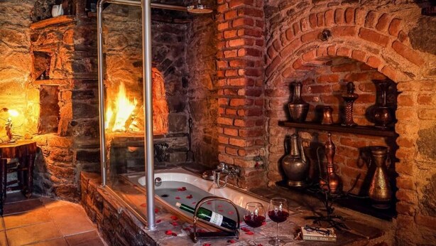 Un bagno con pareti in pietra, una vasca da bagno, un box doccia in vetro e uno scaffale con vasi antichi.