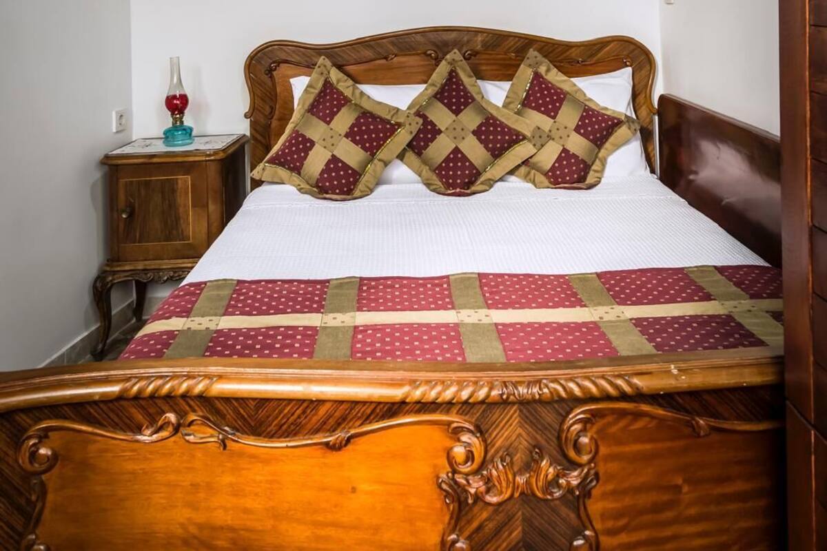 A wooden bed with a quilt, a nightstand with a lamp, and a painting on the wall.