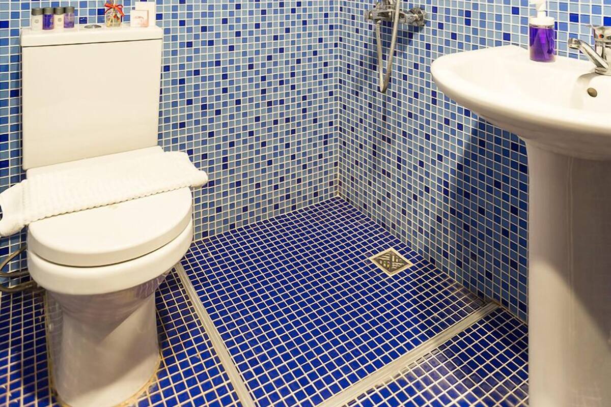A bathroom with a blue mosaic tile wall, a wooden ceiling, a white toilet, a sink, and a shower with a handheld showerhead.