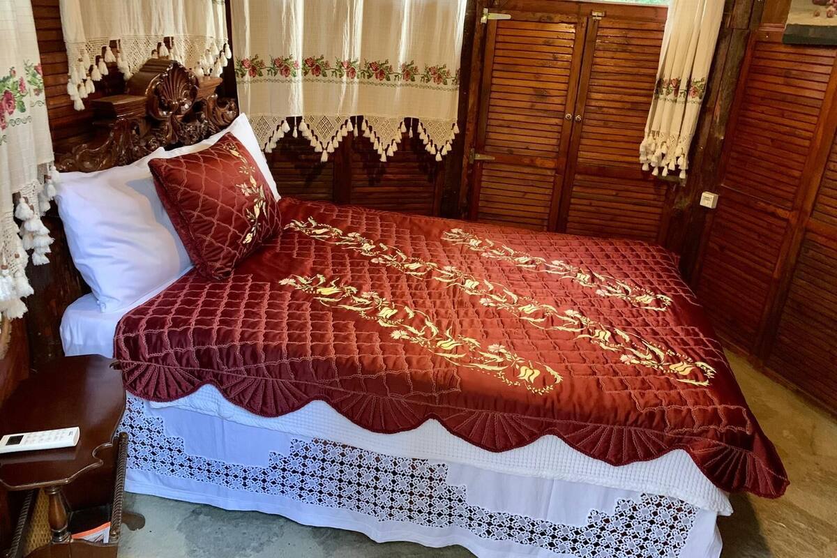 A wooden room with a bed, curtains, and a window.
