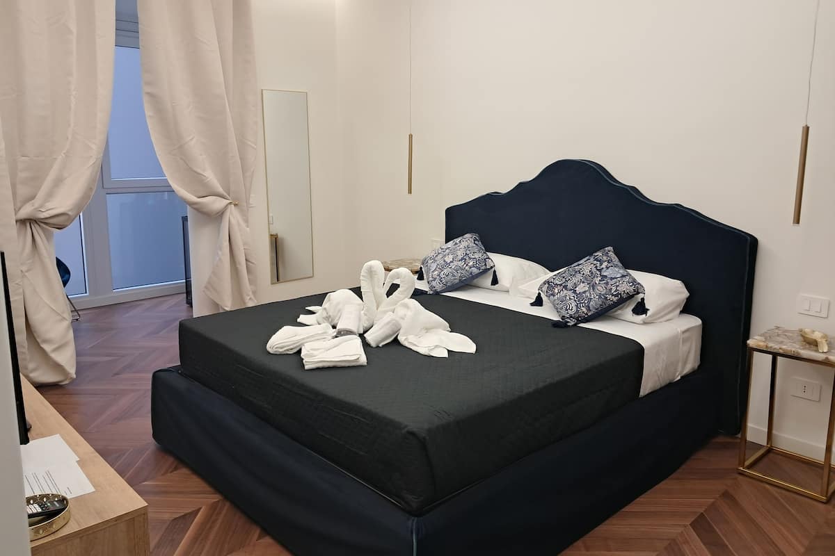 Una cama bien hecha con toallas, un cabecero oscuro, almohadas estampadas y suelo de madera.