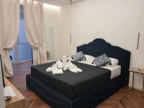 A neatly made bed with towels, a dark headboard, patterned pillows, and a wooden floor. - Sistina Home Collection (Rome)