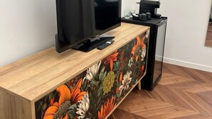 Un salon moderne avec un téléviseur à écran plat posé sur une console en bois, une machine à café et un verre d’eau sur une petite table.