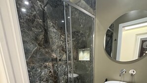 Une salle de bain moderne avec une douche à parois de verre, un lavabo blanc et un sol en marbre.