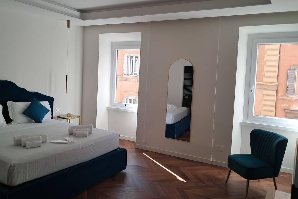Un dormitorio con cama, una silla, un espejo y una ventana.