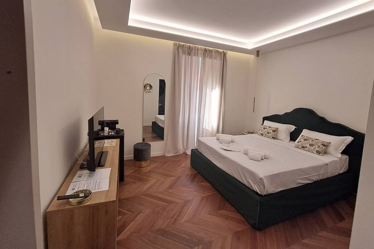 Una habitación de hotel moderna con una cama grande, un escritorio con computadora y un espejo.