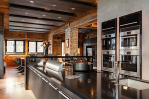 A modern kitchen with a central island, built-in ovens, and a stone accent wall. - Quezac Chalet • Pool, sauna, hot tub • 16 people (Tignes)