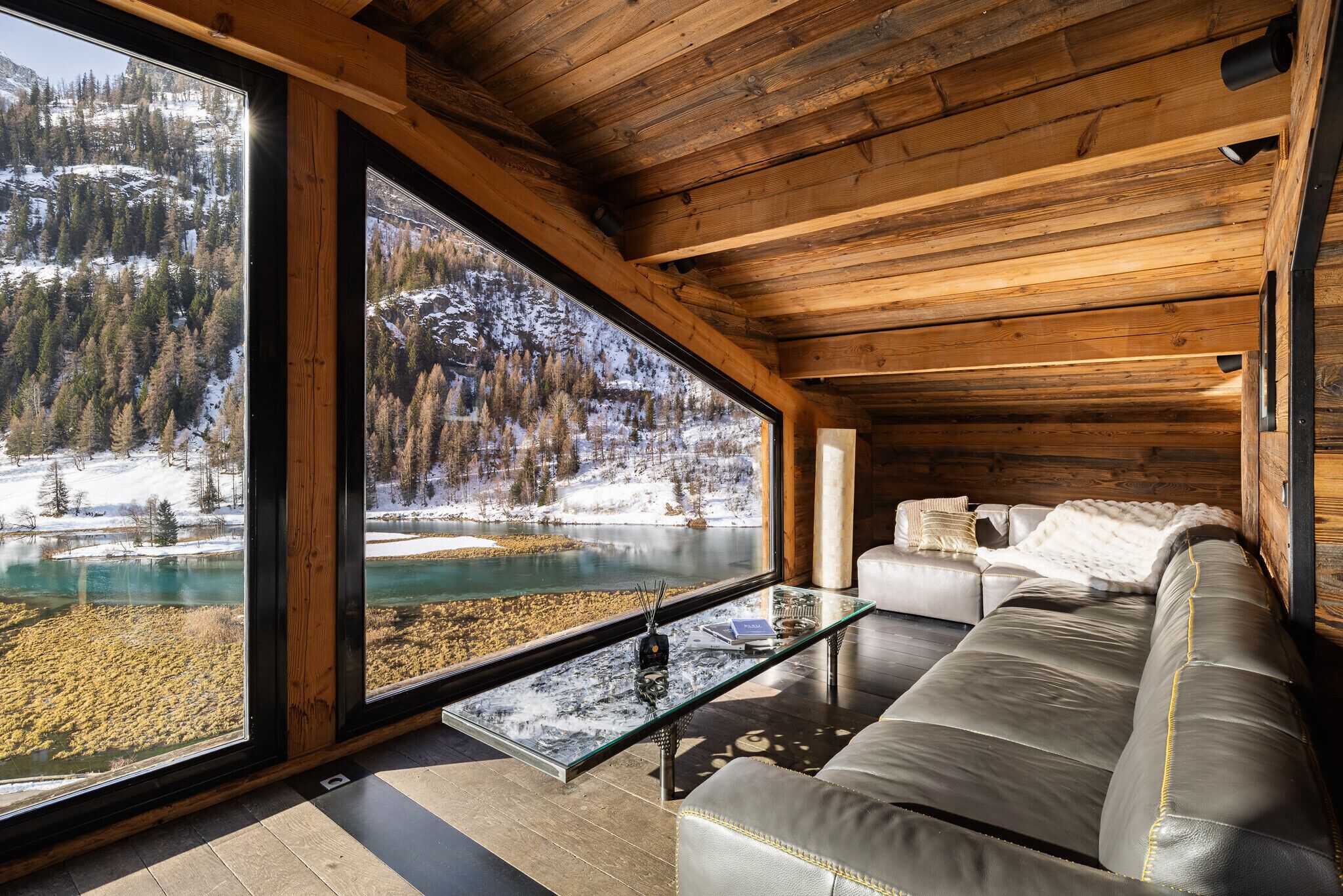 Interior moderno com uma grande janela que oferece vista para uma paisagem nevada e um lago.