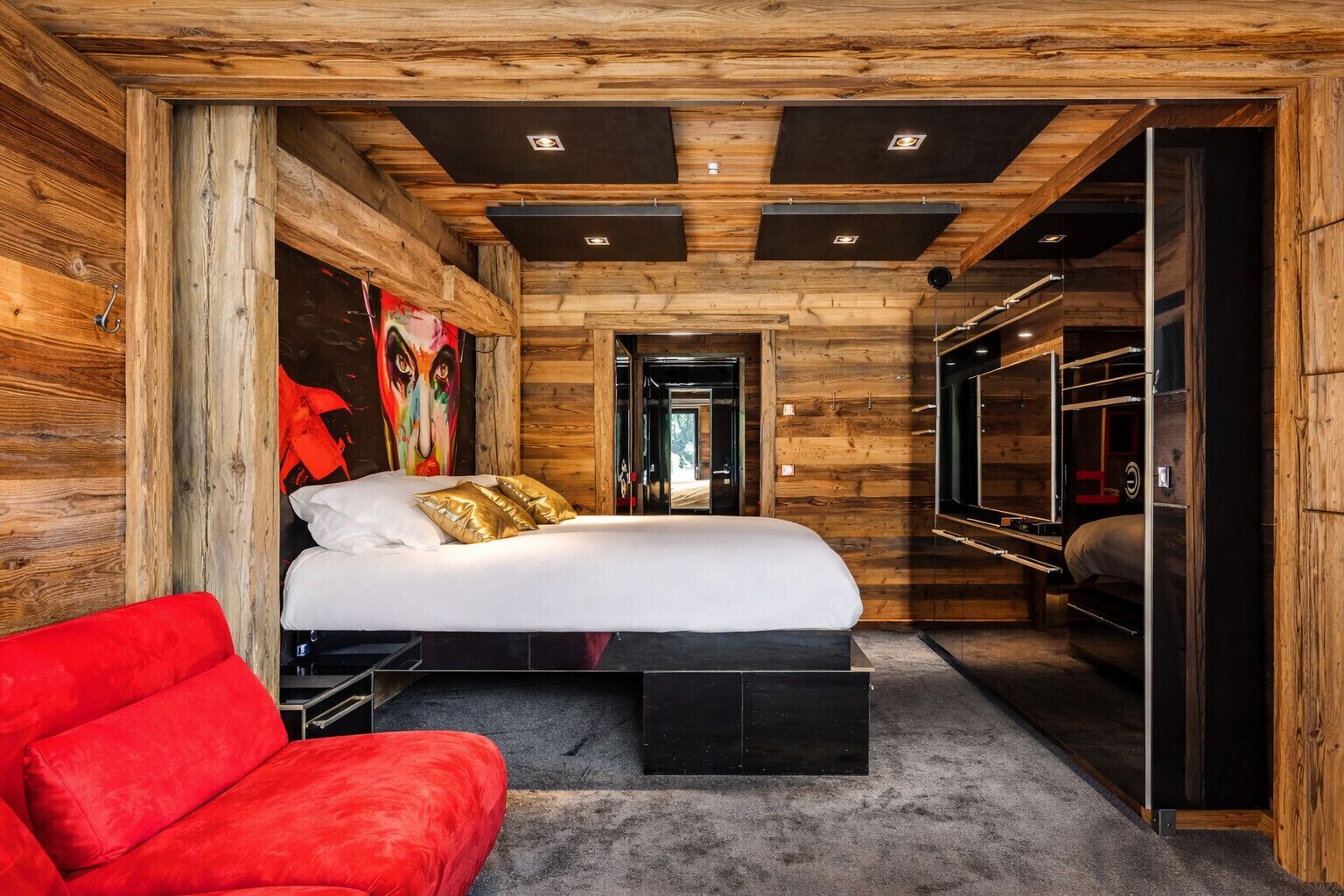 A modern bedroom with a large bed, a red sofa, and a wooden wall.