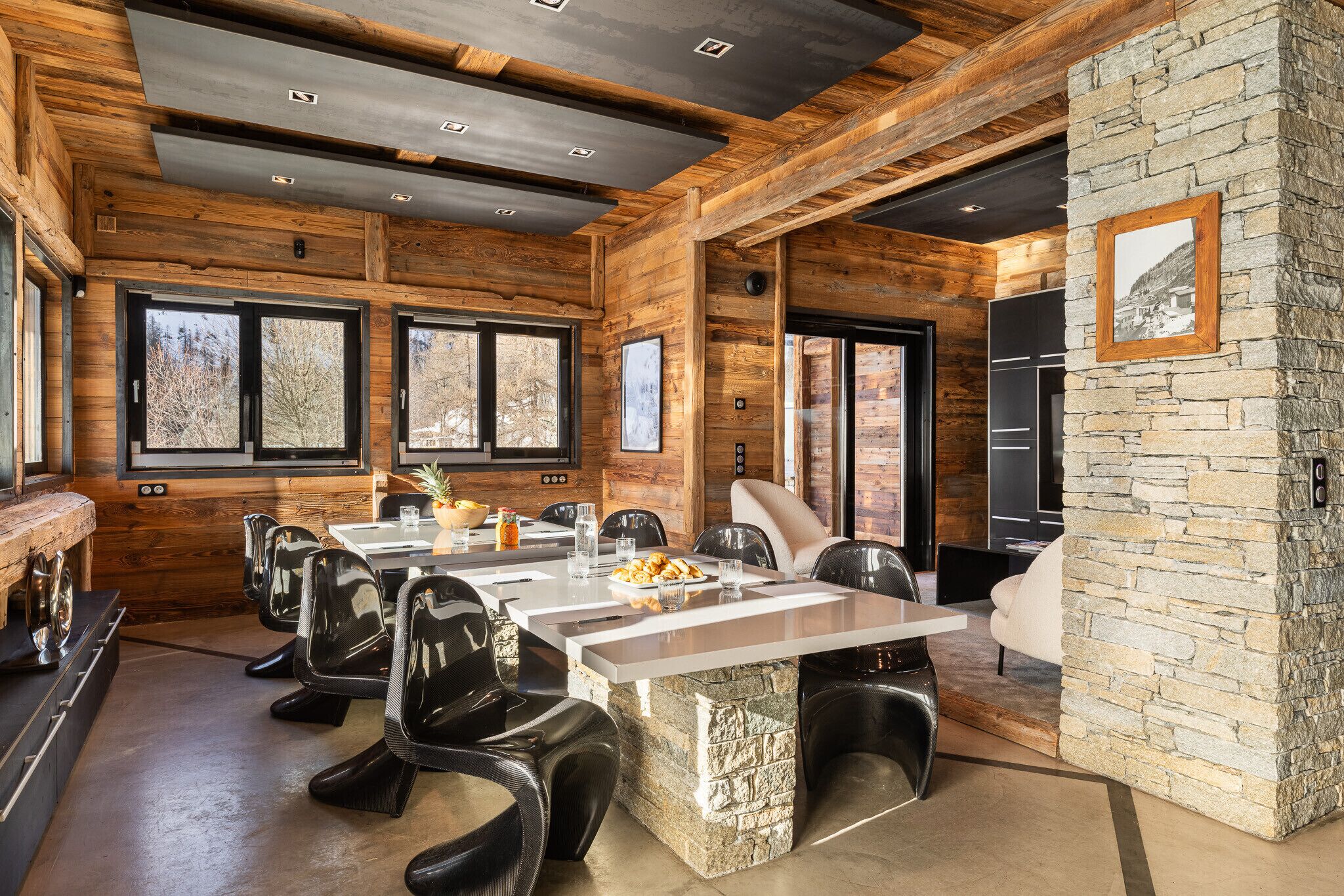 A spacious dining area with a long table, black chairs, and a stone accent wall.