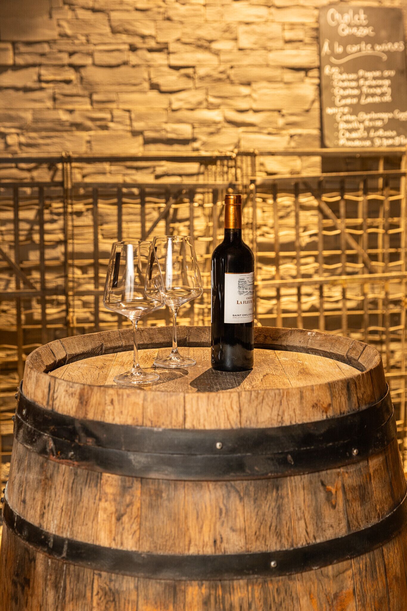 A wooden barrel with a bottle of wine and two wine glasses on top.