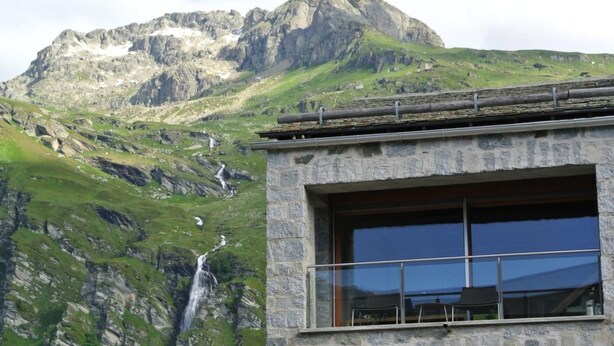 A building with large windows overlooking a mountainous landscape with a waterfall. - La Montanella 4 by Interhome (Maloja)