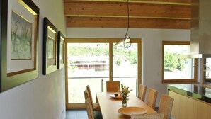 A dining area with a wooden table and chairs, large windows, and framed artwork on the walls. - La Montanella 4 by Interhome (Maloja)