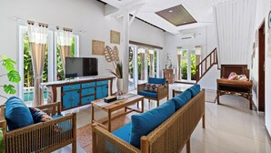A spacious living area with a wooden sofa, a coffee table, and a television. There is a wooden cabinet with blue doors and a staircase leading to another level. - Canggu Wave Villa (Canggu)