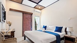 A hotel room with a large bed, a wooden nightstand, a wicker chair, and a ceiling fan. - Canggu Wave Villa (Canggu)