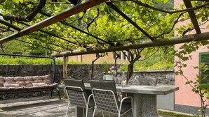 Un espacio al aire libre con asientos de piedra, una mesa y sillas, rodeado de follaje y un muro de piedra.