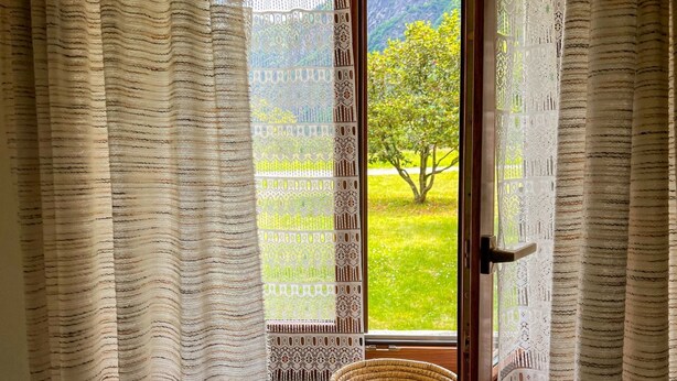 Una habitación con vistas a través de una ventana con cortinas estampadas, una cesta de mimbre en el alféizar y una puerta con un cierre.