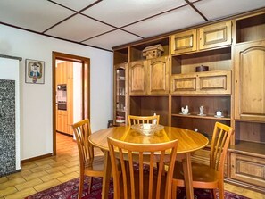 Comedor con mesa y sillas de madera, alfombra roja con diseño y armarios de madera con cristalería.