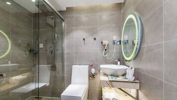 Un baño moderno con ducha de vidrio, inodoro blanco, un espejo ovalado grande y un mueble de tocador con lavamanos y toallero.