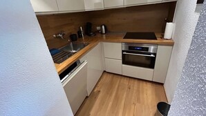 Una cocina compacta con armarios blancos, encimera de madera, horno empotrado y lavavajillas.