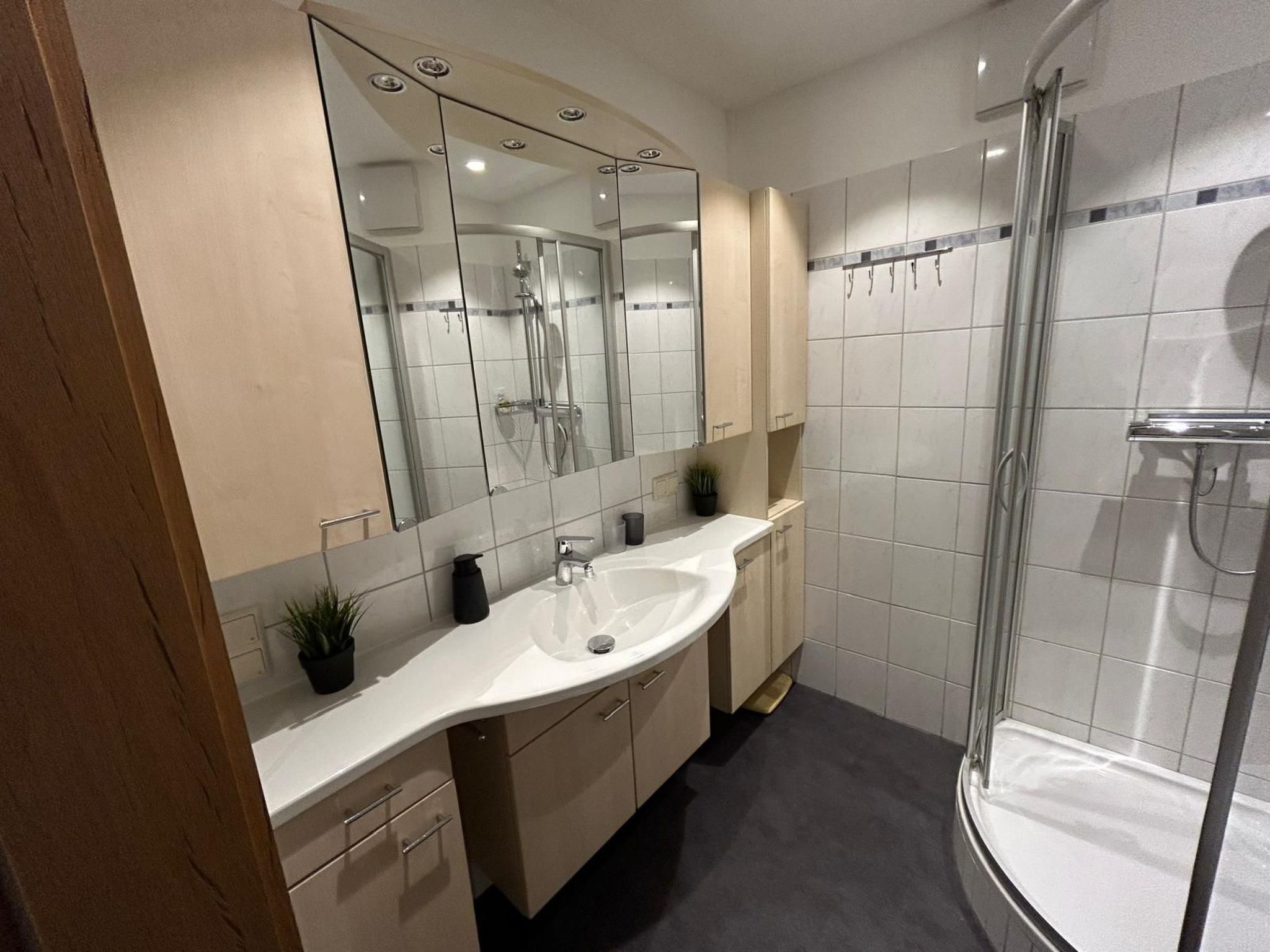 Ein modernes Badezimmer mit einem großen Spiegel, einem weißen Waschbecken und einer Duschkabine aus Glas.
