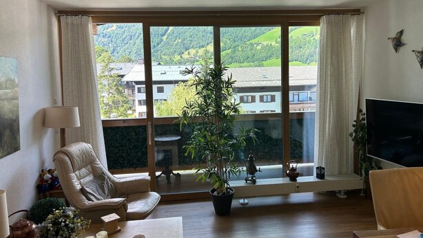 Una sala de estar con un ventanal grande, un sofá, un televisor y una planta en maceta.