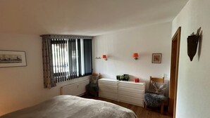 Un dormitorio con una cama, un tocador, un radiador y una ventana con cortinas.