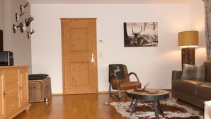 A living room with a wooden door, a brown leather chair, a sofa, a cowhide rug, and a lamp. - Wohnung Alpinresort Kaprun top 11 by Interhome (Kaprun)