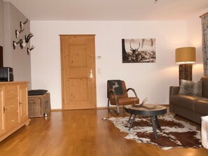 A living room with a wooden door, a brown leather chair, a sofa, a cowhide rug, and a lamp. - Wohnung Alpinresort Kaprun top 11 by Interhome (Kaprun)