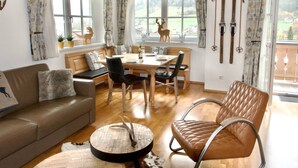 A cozy living room with a sofa, a round coffee table with antlers, a dining area with a table and chairs, and a window with a view of the outdoors. - Wohnung Alpinresort Kaprun top 11 by Interhome (Kaprun)