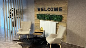 Een receptiegedeelte met twee beige fauteuils, een kleine tafel en een 'WELCOME'-bord aan de muur.