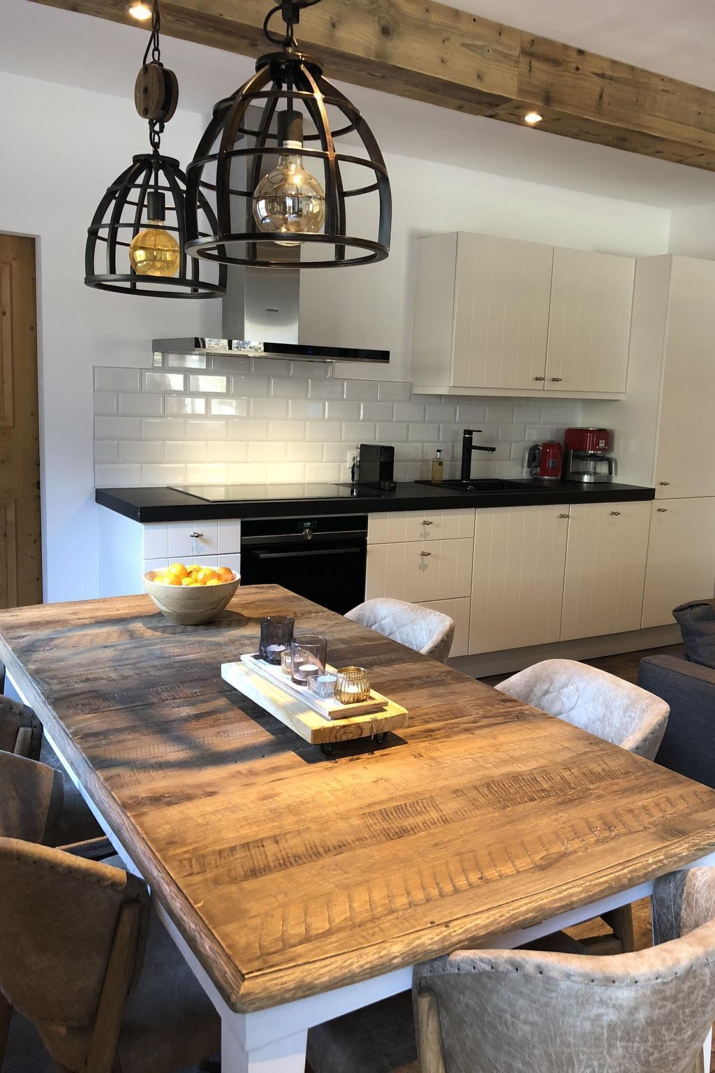 A modern kitchen with a wooden dining table, white cabinets, and pendant lighting.