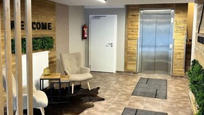Een moderne lobby met een receptiebalie, een zithoek en een lift.