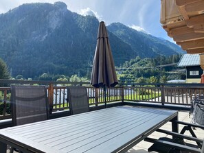 Eine Terrasse mit Tisch und Stühlen, einem braunen Sonnenschirm und Blick auf die Berge.