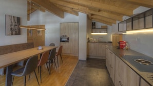 A modern kitchen with wooden beams, a dining area with chairs, and a kitchen island with a sink. - Penthouse Alpinresort Kaprun oben 14 by Interhome (Kaprun)