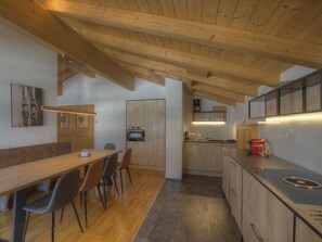 Eine moderne Küche mit Holzbalken, einem Essbereich mit Stühlen und einer Kücheninsel mit Spüle.