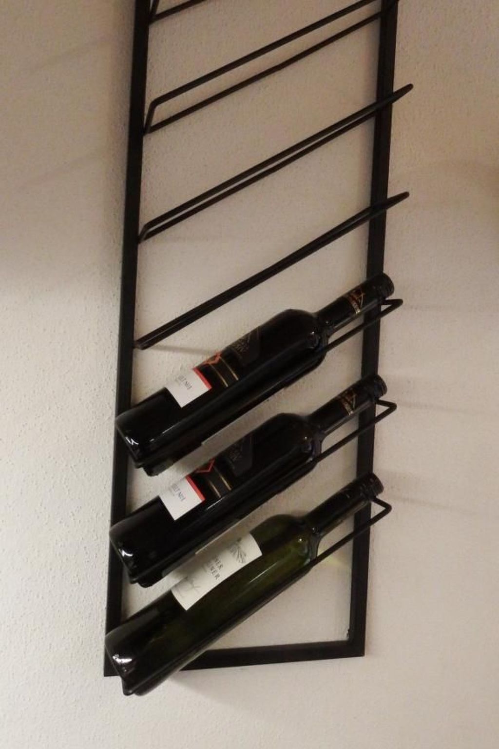 En vinskab med fire flasker op ad en væg.