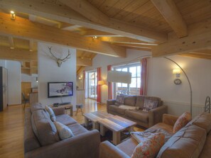 Ein geräumiges Wohnzimmer mit Holzbalken, einem Fernseher, einem Sofa und einem Couchtisch.