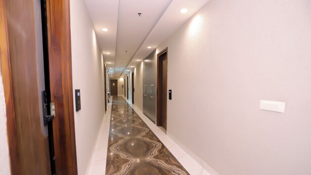 A hallway with a marble floor, wooden doors, and white walls. - Hotel Nirvana Inn Near Expo Center (Greater Noida)