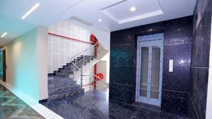 A modern interior with a marble staircase, a glass elevator, and a tiled floor. - Hotel Nirvana Inn Near Expo Center (Greater Noida)