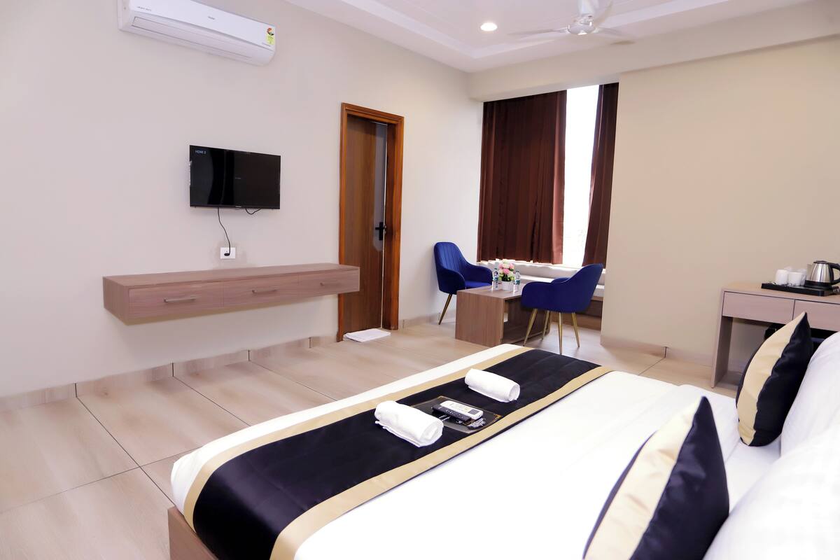A hotel room with a bed, a desk, a chair, a TV, and a minibar.