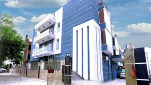 A modern multi-story building with a prominent blue and white facade, large windows, and a gated entrance. - Hotel Nirvana Inn Near Expo Center (Greater Noida)