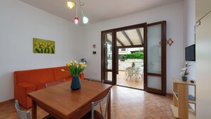 Ein Essbereich mit Holztisch, orangefarbenem Sofa und einem Blumenstrauß. Eine Schiebetür aus Glas führt zu einer Außenpatio.