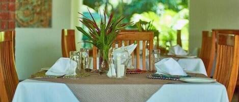 A dining table set with white tablecloths, wooden chairs, and a central plant.
