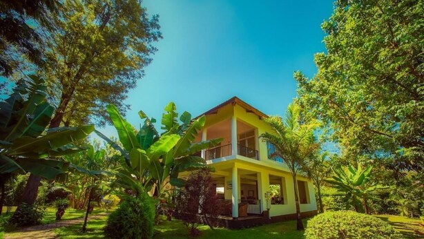 Un bâtiment à deux étages doté d’un balcon, entouré d’une végétation luxuriante et d’arbres.