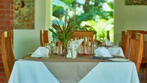 Une table à manger recouverte d’une nappe blanche, avec des chaises en bois et une plante en pot.
